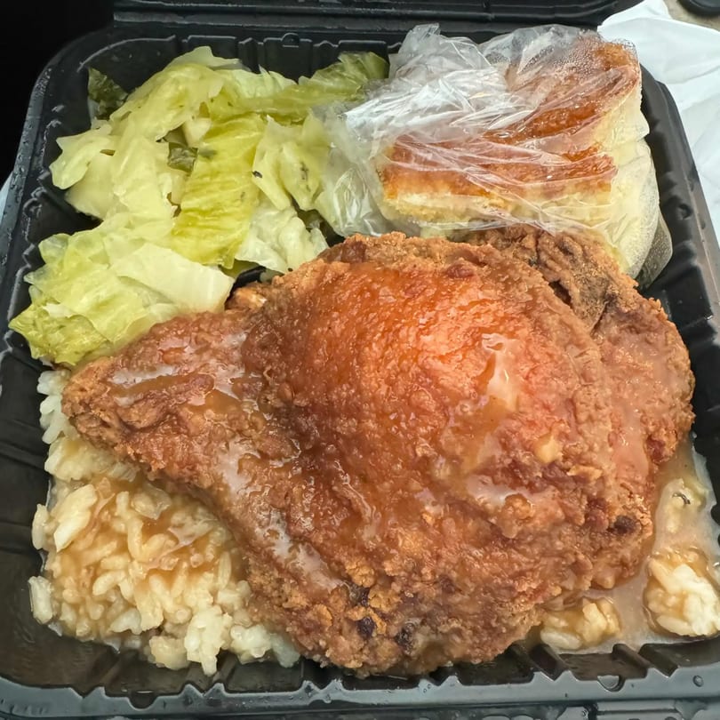 Dakari Soul Food's fried chicken with gravy, rice, and lettuce in a black takeout container.
