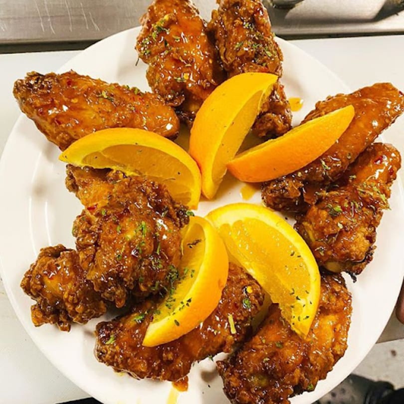 A plate of Dakari Soul Food's sticky orange chicken wings garnished with fresh orange slices.