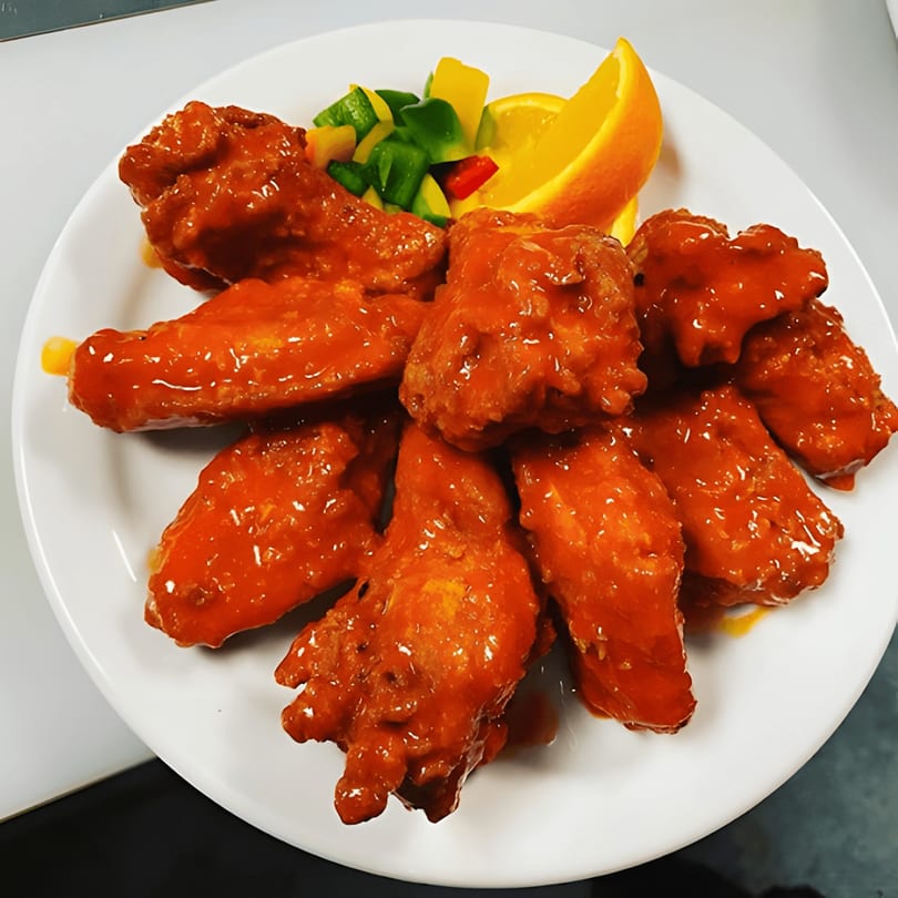 Dakari Soul Food's buffalo wings, glistening with sauce, garnished with bell peppers and an orange slice.
