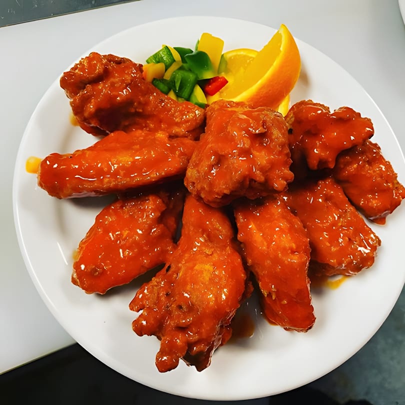 A plate of Dakari Soul Food's orange-glazed chicken wings with bell peppers and an orange slice.